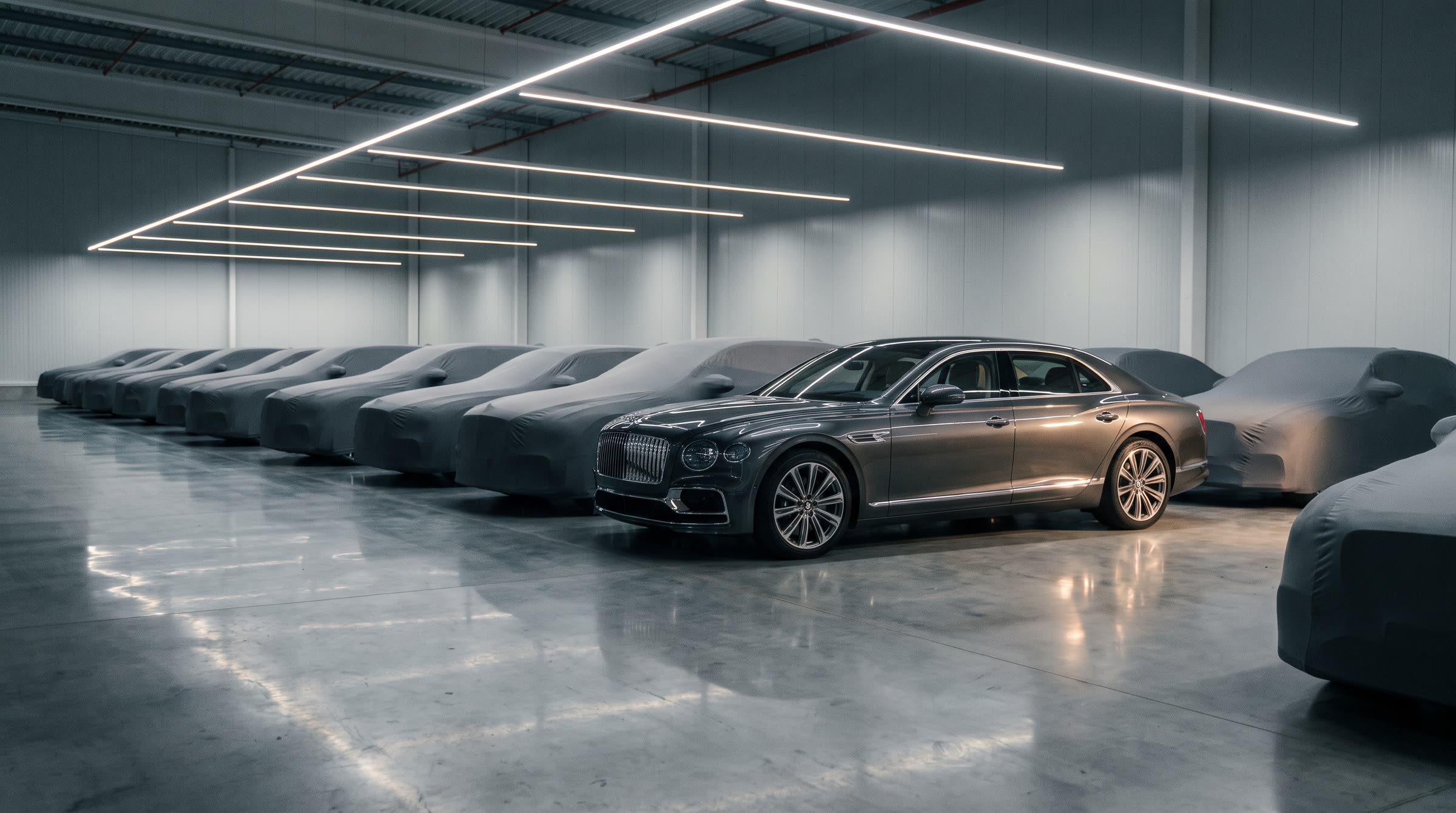 Interior de una nave de custodia de vehículos con coches cubiertos con fundas y una berlina de lujo descubierta en primer plano.